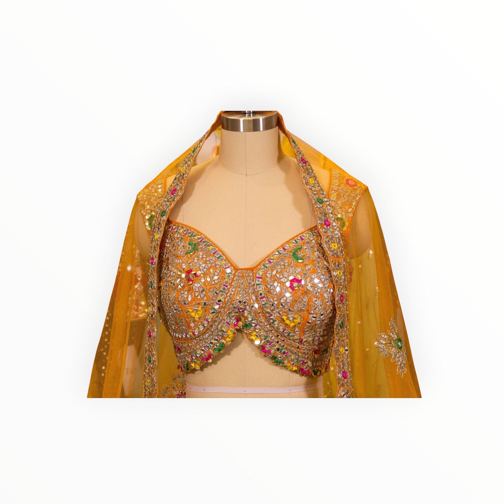 Zari Designs Carnival Lehnga featuring a vibrant orange blouse with intricate mirror work and colorful embroidery.